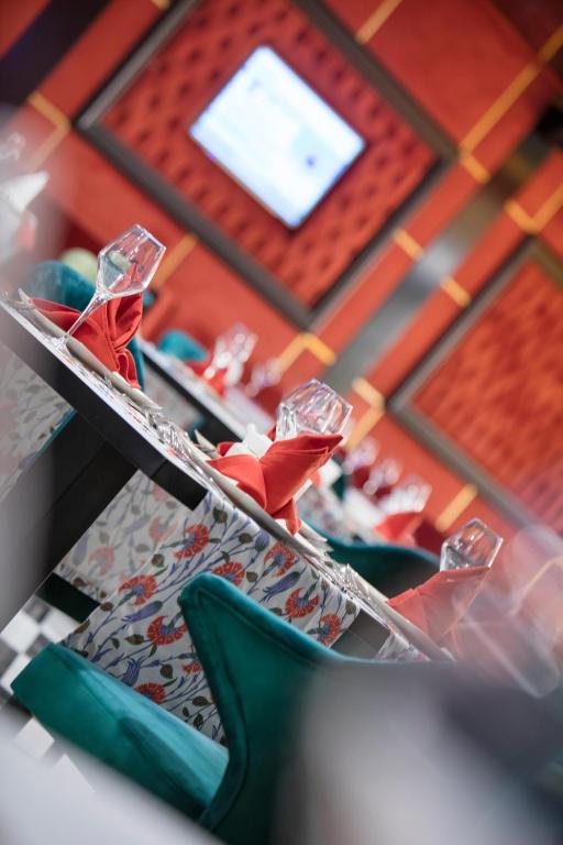 Elegants restorāna interjers ar krāsainām galda klājumam, kas ietver sarkanas salvetes un glāzes, izceļot modernu atmosfēru. Fons papildina sarkanas un dzeltenas krāsas akcenti.