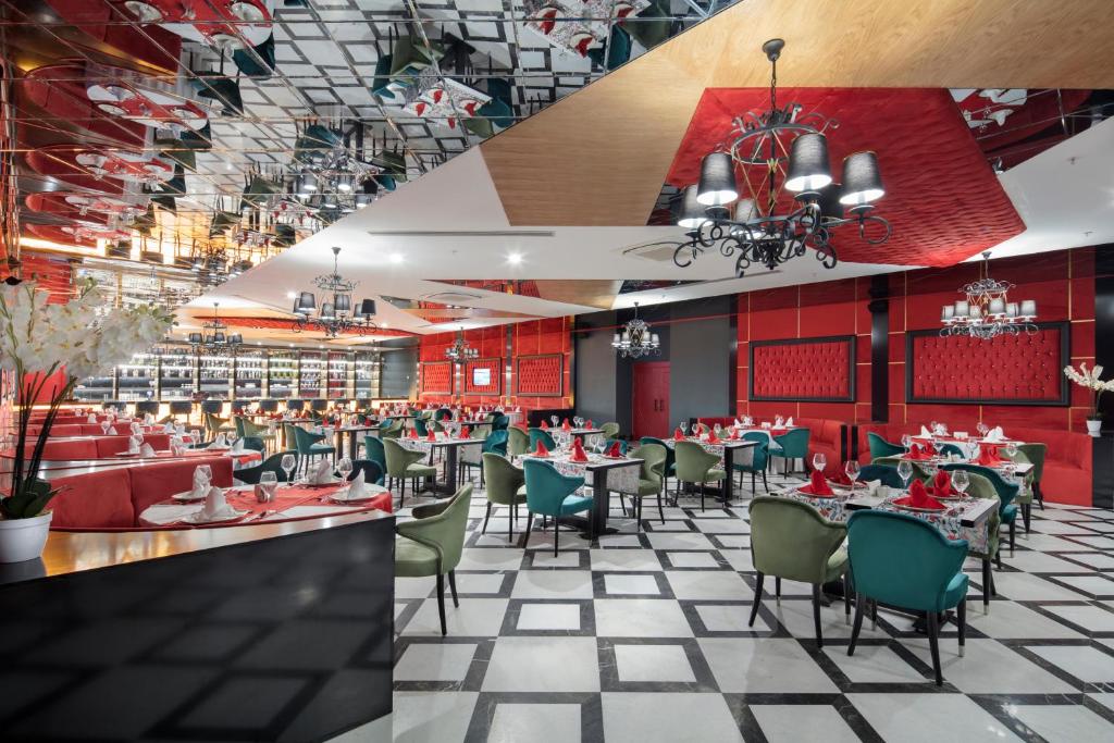 Mūsdienīgs restorāna interjers ar elegantiem galdiem un krēslām, sarkaniem akcentiem un greznām gaismām. Atspoguļota griestu konstrukcija rada unikālu atmosfēru.