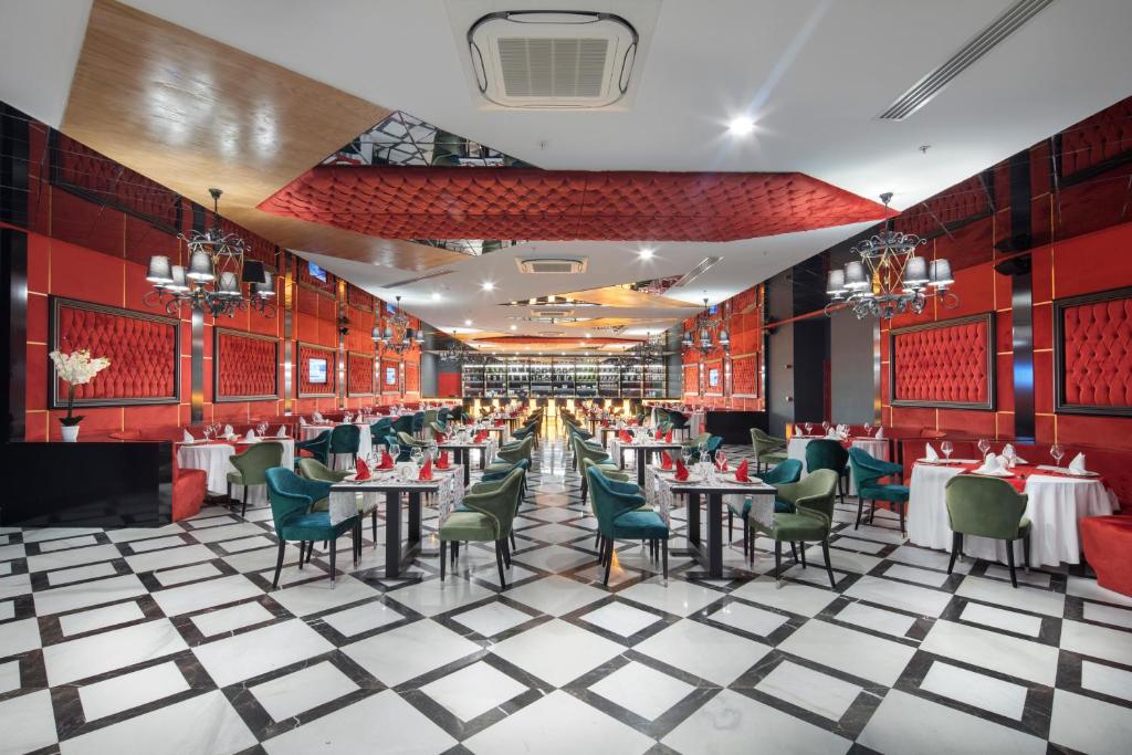 Eleganta restorāna iekārtojums ar sarkaniem un zaļiem krēsliem, melnbalto grīdu un izsmalcinātiem galdiem. Telpa ir gaiša un moderni iekārtota, piebūvējot krāšņas lampas un dekorācijas.