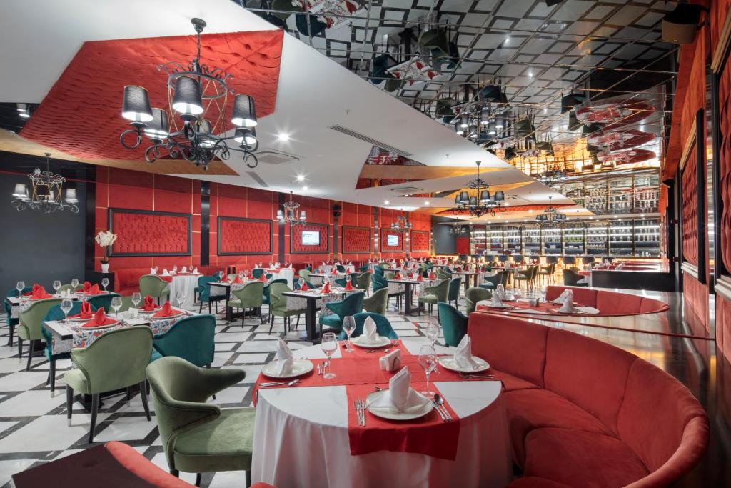 Mūsdienīga restorāna interjers ar sarkaniem un zaļiem krēsliem, eleganti klātiem galdiem un stilīgiem gaismekļiem. Telpa izceļas ar modernu dizainu un spoguļotām griestiem.