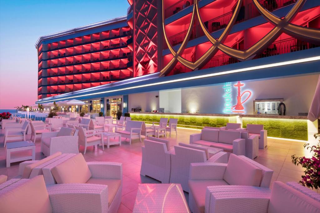 Mūsdienīgs viesnīcas terases skats ar baltām mēbelēm un sarkanām apgaismojuma detaļām, kas rada stilīgu un viesmīlīgu atmosfēru.