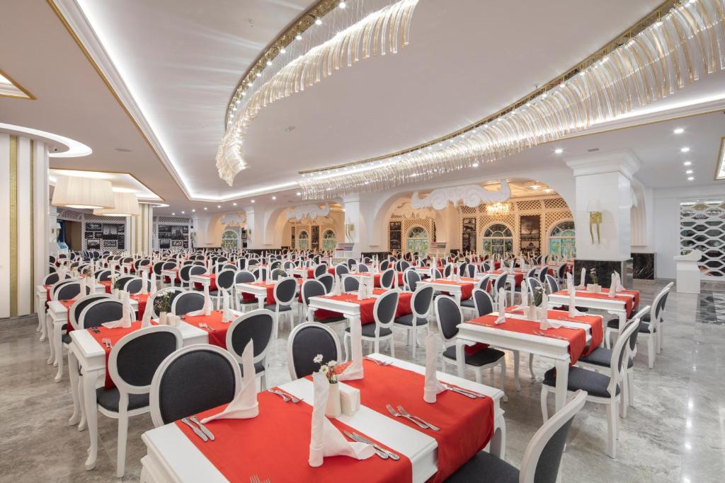 Mūsdienīgs restorāns ar elegantiem galdiem un sarkanām galdautām, kas izkārtoti plašā telpā ar greznu apgaismojumu.