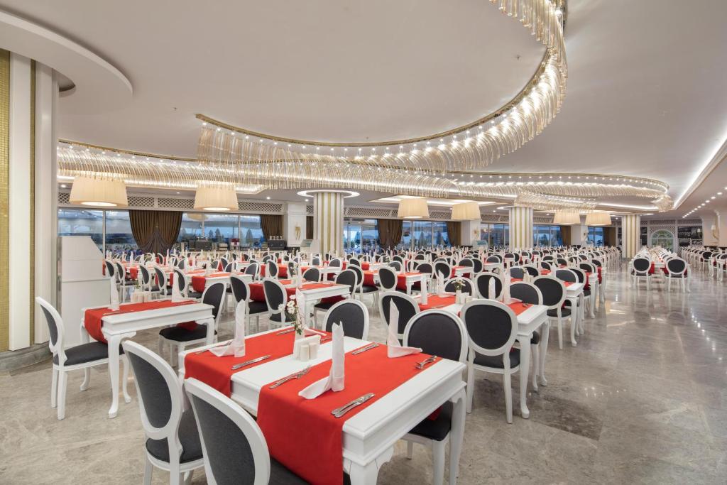 Elegants restorāns ar baltām mēbelēm un sarkaniem galda palikņiem, kas rada modernu un stilīgu atmosfēru. Gaismas ķermeņi un plašas logu vitrīnas piešķir telpai dzīvīgumu un komfortu.