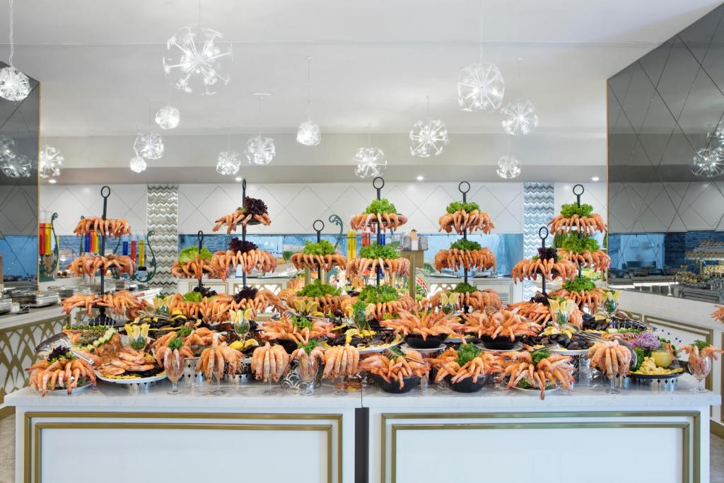 Bagātīgs jūras velšu bufete ar garnelēm, kas dekorēta ar zaļumiem un citām uzkodām, izstādīta modernā restorāna interjerā. Gaismas ķermeņi rada elegantu atmosfēru.