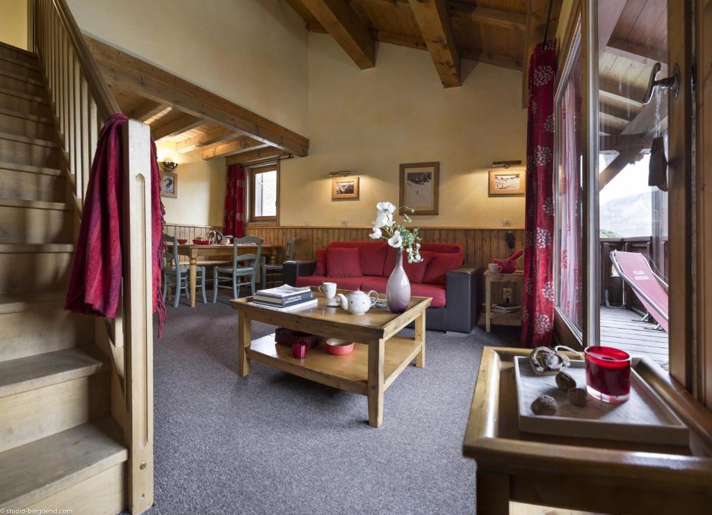 Moderna un mājīga viesistaba ar koka apdari, sarkanu dīvānu un ēdamgaldu, kas veido patīkamu atmosfēru. Logi piedāvā skatu uz ārpusi, radot siltu un viesmīlīgu noskaņu.