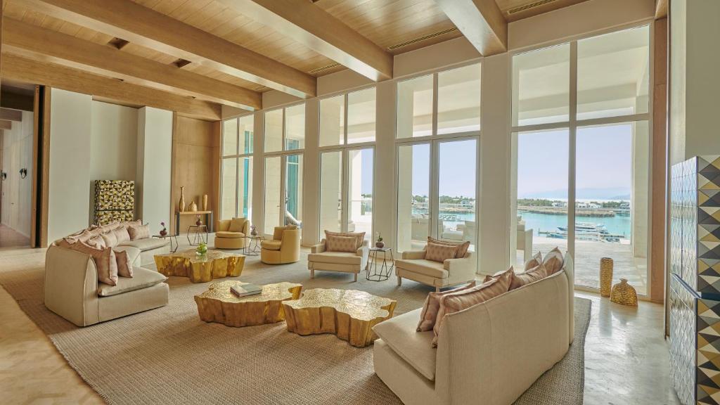 Mūsdienīgs viesistabas interjers ar plašiem logiem, kas piedāvā skatu uz ūdeni. Telpā ir ērti dīvāni un unikālas koka kafijas galdiņi, radot elegantu un relaksējošu atmosfēru.