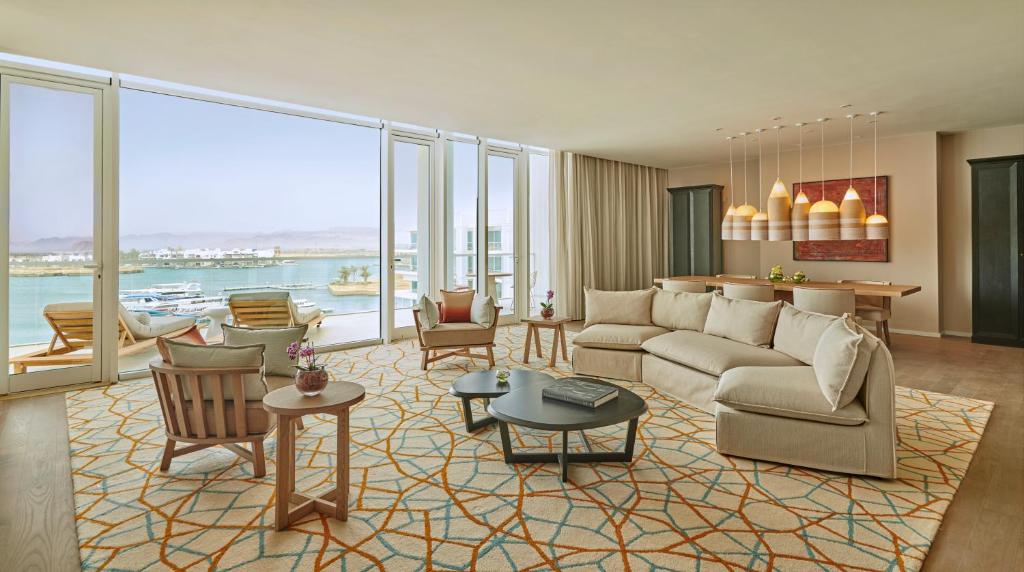 Mūsdienīgs viesistabas interjers ar plašiem logiem, kas sniedz skatu uz ūdeni. Interjers ir veidots ar gaišām krāsām un elegantiem mēbeļu elementiem, radot ērtu un relaksējošu atmosfēru.