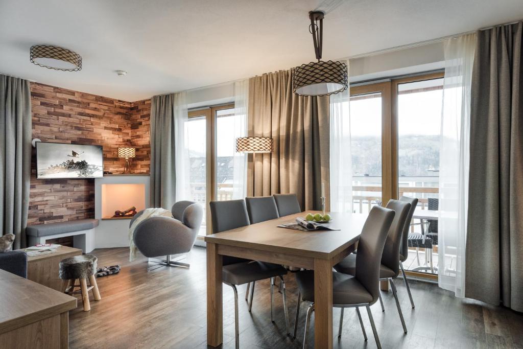 Mūsdienīgs viesistabas interjers ar koka akcentiem, apgaismojumu un ērtu mēbelējumu, kas nodrošina patīkamu atmosfēru. Lielas logu ailes sniedz dabisko apgaismojumu un skatu uz ārpusi.