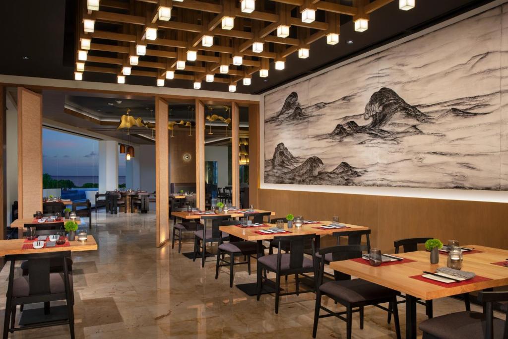 Moderns restorāns ar stilīgu interjeru, koka detaļām un māksliniecisku sienas gleznojumu, kas attēlo kalnu ainavas. Skats uz jūru un eleganti klāti galdi rada patīkamu atmosfēru.