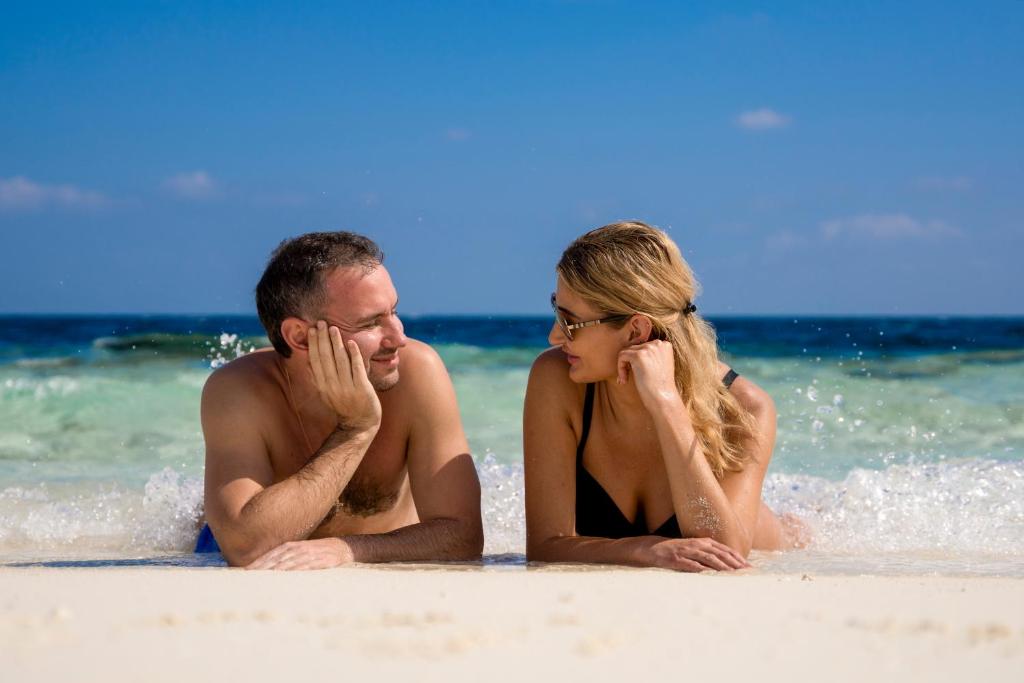 Pāris izbauda saulainu pludmales dienu, guļot uz smiltīm un sarunājoties, kamēr viļņi maigi skar krastu.