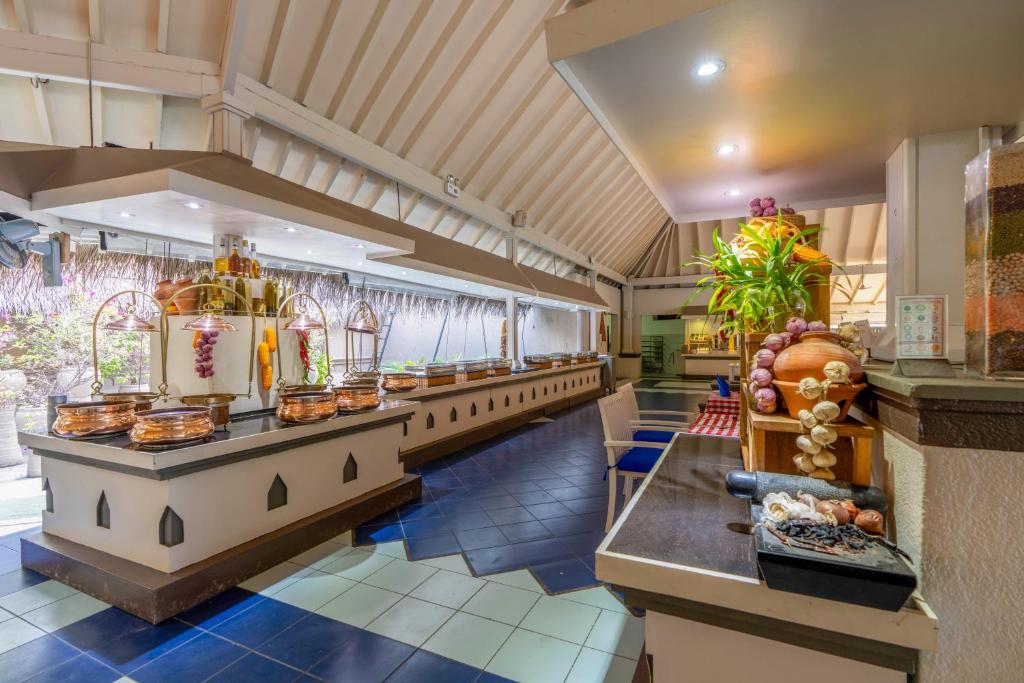 Labi iekārtota bufete ar dažādiem ēdieniem un garšvielām, gaišā restorāna vidē ar augstiem griestiem un dabīgu apgaismojumu.