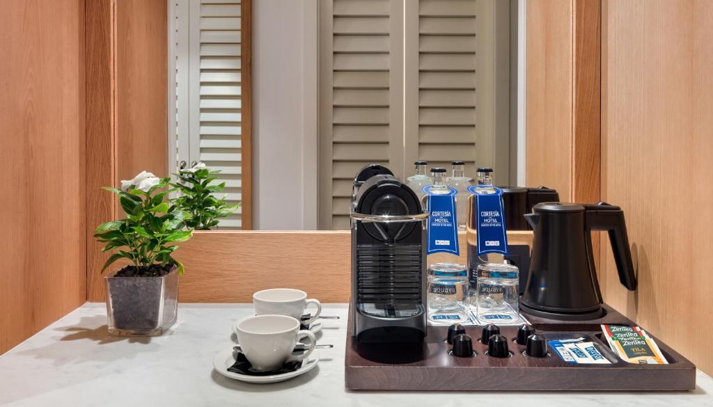 Kafijas stūrītis ar Nespresso aparātu, glāzēm un ūdens pudelēm, ko papildina dekoratīvs augs. Ideāli piemērots relaksācijai un uzmundrināšanai.