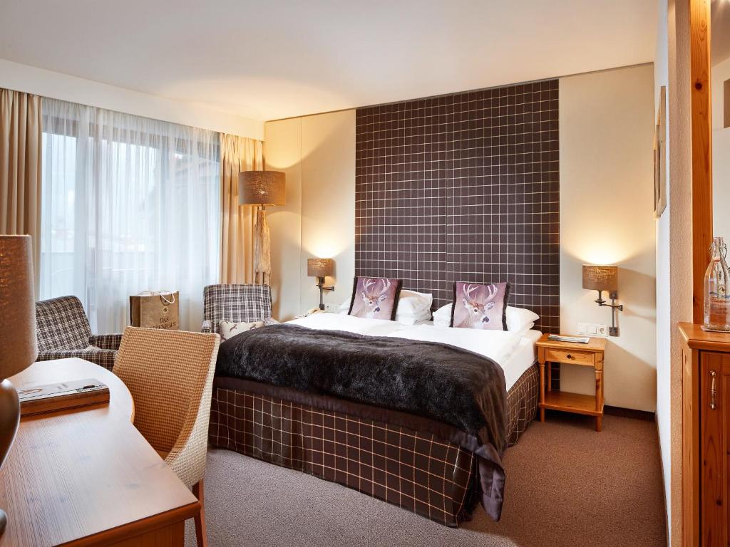 Mūsdienīgs guļamistabas interjers ar ērtu gultu, stilīgu apgaismojumu un sēdvietām. Telpa ir gaiša un aicinoša, ar mīkstām tekstūrām un moderniem akcentiem.