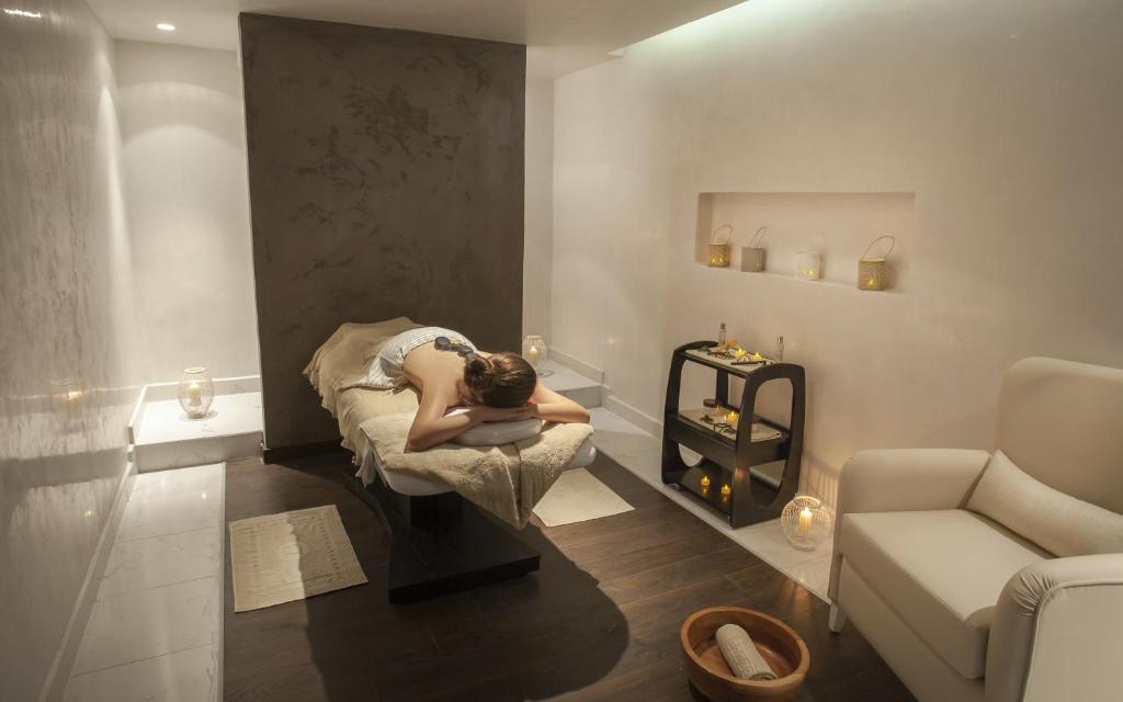 Relaksējoša masāžas telpa ar mierīgu atmosfēru, kurā redzams cilvēks, kas guļ uz masāžas galda. Telpā ir zemas gaismas un dekoratīvas sveces, radot atpūtu veicinošu noskaņu.