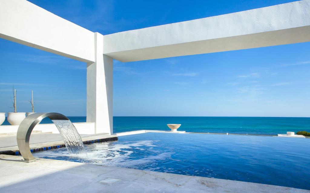 Mūsdienīga viesnīcas baseina zona ar skatu uz jūru, kurā ir stilizēts ūdens kritums un plaša debesskrāsa. Ideāla vieta relaksācijai un atpūtai.