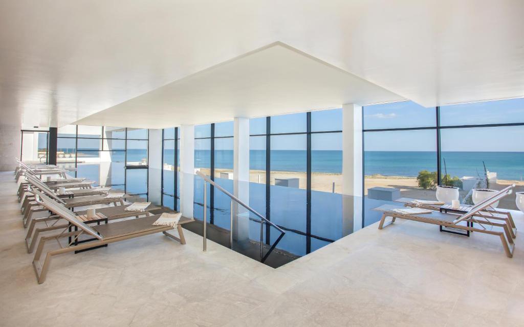 Mūsdienīgs atpūtas telpa ar skatu uz jūru, kurā ir saules krēslas un komfortabli atpūtas krēsli. Labi apgaismota telpa ar lieliem logiem, kas nodrošina dabisku gaismu un relaksējošu atmosfēru.