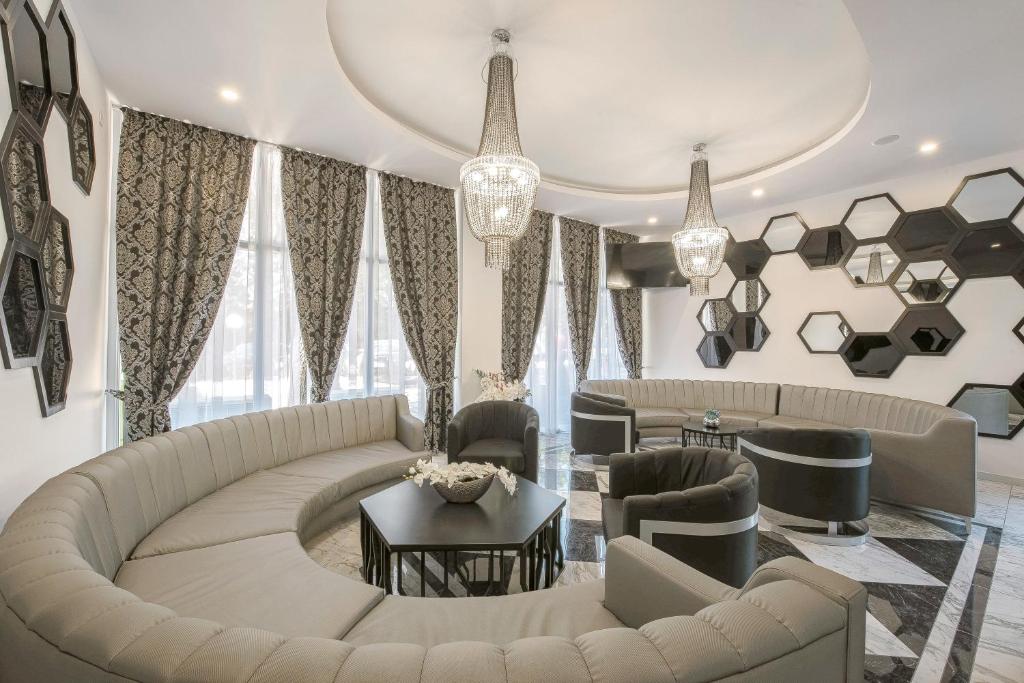 Elegants interjers ar pelēku dīvānu un modernām lampām, kas rada stilīgu atmosfēru. Telpā ir lieli logi un dekoratīvas spoguļu formas uz sienām.