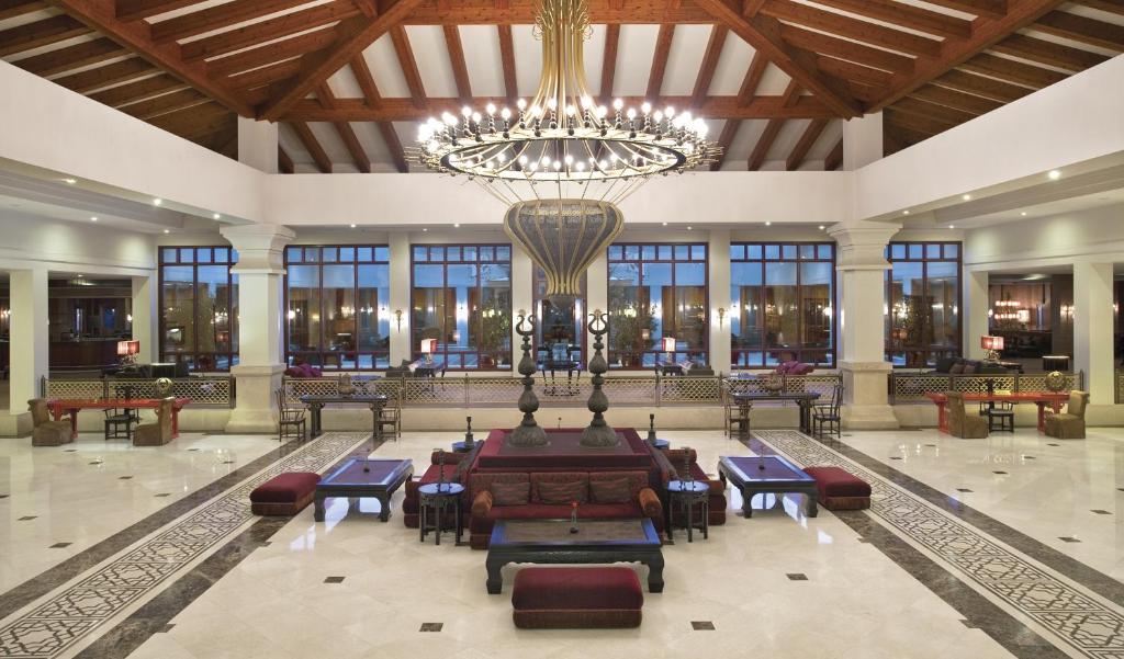 Lieliska viesnīcas uzgaidāmā telpa ar modernas arhitektūras elementiem, koka griestiem un greznu lustru. Plašas logu ailes nodrošina dabisko apgaismojumu un brīvu atmosfēru.