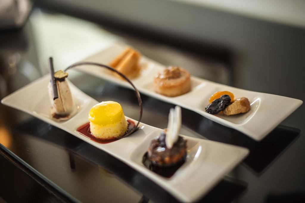 Elegants deserts uz baltām šķīvīšiem, kas ietver dažādas konfektes un kūkas, apvienojot krāsainus un izsmalcinātus elementus. Ideāli piemērots gardēžu baudījumiem.