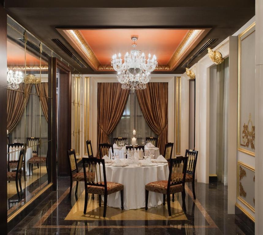 Eleganta restorāna interjers ar greznām aizkariem, kristāla lustru un izsmalcinātu galdu, kas sagatavots svinīgām maltītēm. Iekārtojums rada romantisku un stilīgu atmosfēru.