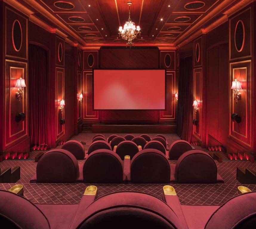 Mūsdienīga kino zāle ar sarkaniem toņiem, ērtām sēdvietām un lielu ekrānu, radot intīmu un greznu atmosfēru.