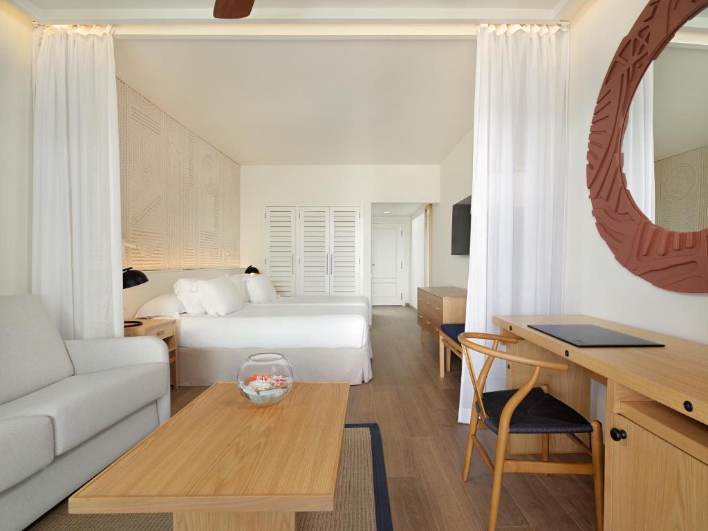 Mūsdienīgs viesnīcas numurs ar gultu, dīvānu un koka galdu. Interjerā ir viegla krāsu palete un dekoratīvi elementi, radot relaksējošu atmosfēru.