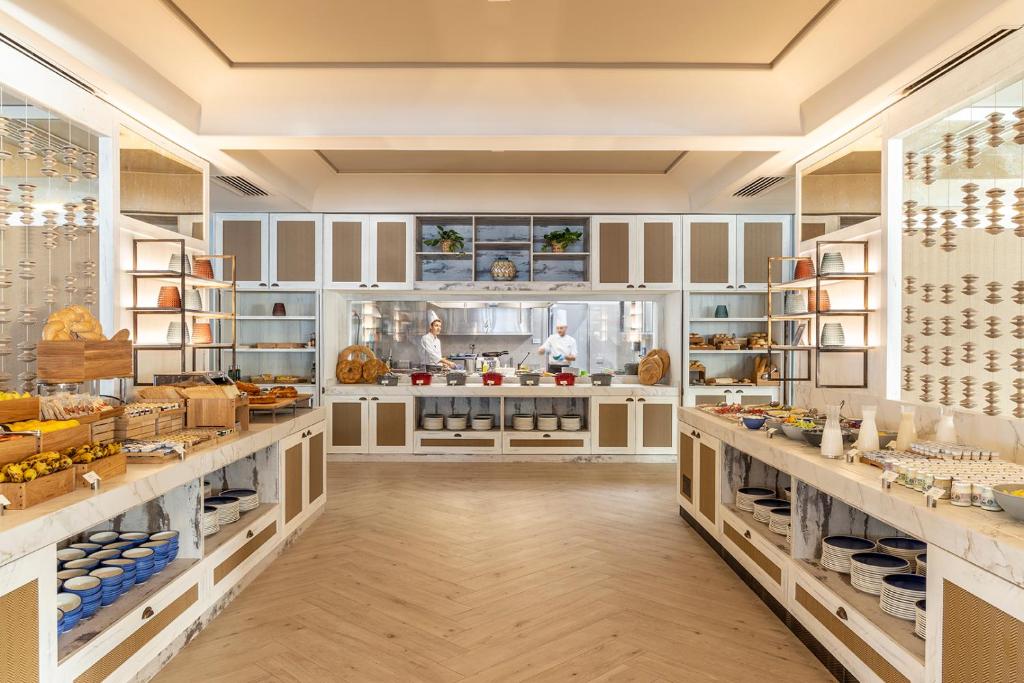 Mūsdienīga restorāna virtuve ar plašu ēdienu klāstu, iekārtota ar elegantiem mēbeļu elementiem un koka plauktiem. Šefpavāri strādā virtuvē, sagatavojot gardumus.