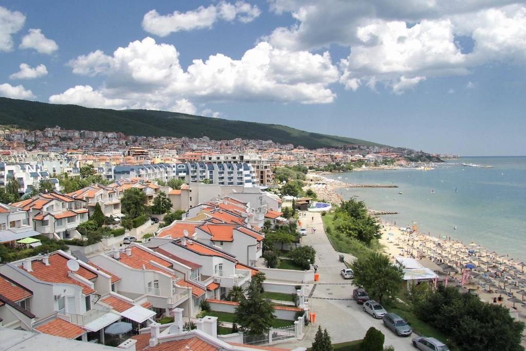 Skats uz piekrastes pilsētu ar pludmali, kas ieskauta zaļiem kalniem un mājām ar sarkanajiem jumtiem. Mierīga jūra un daudzas saulainas pludmales vietas.