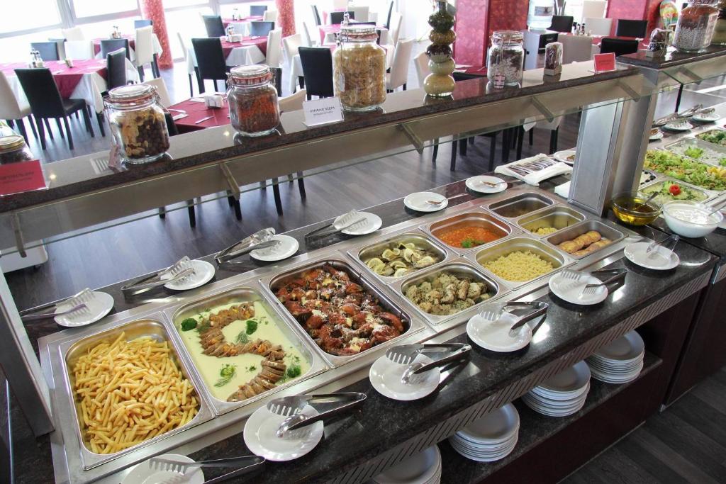 Bufete ar dažādiem ēdieniem, tostarp makaronu, dārzeņu, gaļas un salātu izvēle, kas pasniegta viesnīcā. Jauka pārtikas prezentācija ar ērtām šķīvju un galda piederumu iespējām.