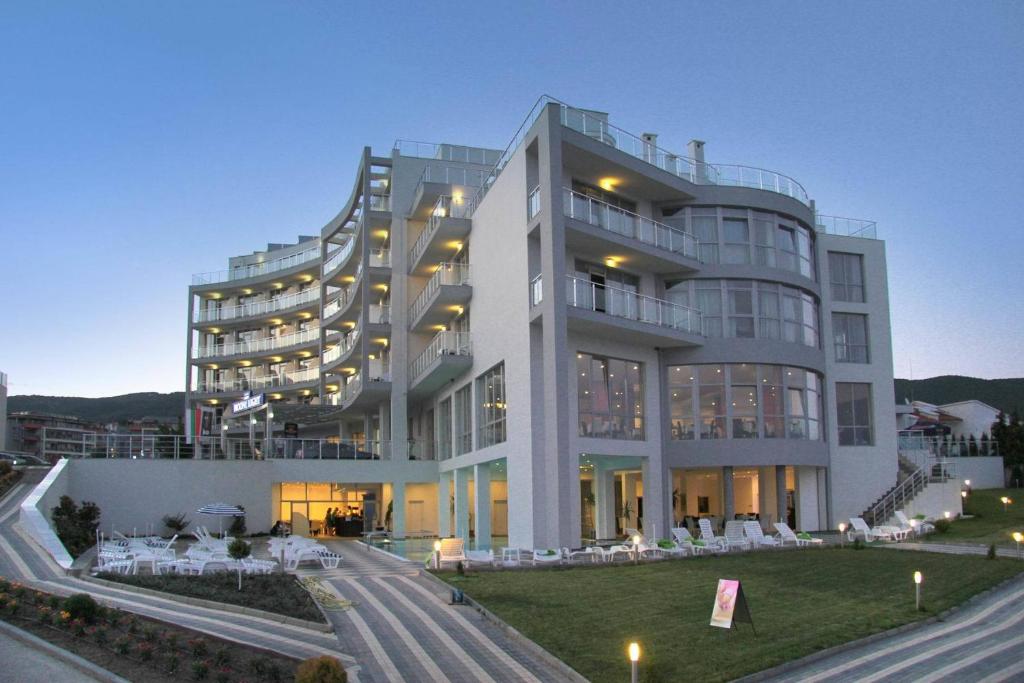 Mūsdienīgs viesnīcas ēka ar plašām terasēm un stiklotām fasādēm, apgaismota vakarā. Apkārtnē redzami sauļošanās krēsli un zāliens.