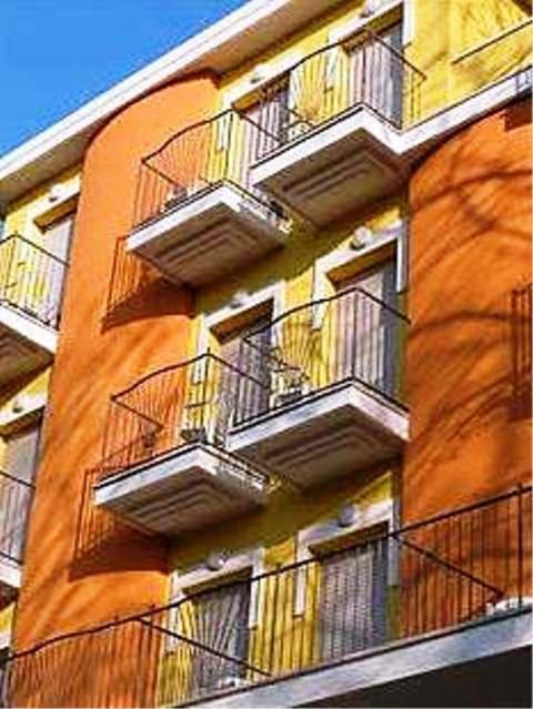 Krāsains ēkas fasāde ar dzeltenu un oranžu krāsu, izceļot balkonus un metāla margas. Šī attēla arhitektūra piedāvā modernu un dzīvīgu atmosfēru.