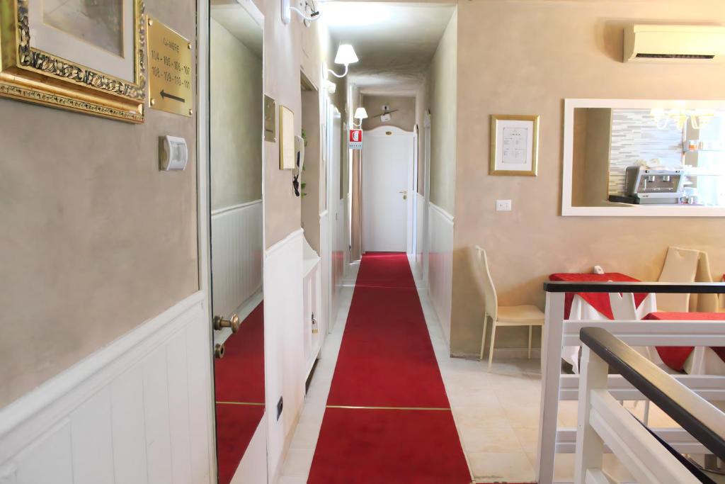 Sarkanas paklājas viesnīcas koridorā ar dekoratīviem elementiem un piekļuvi telpām. Gaismas un mūsdienīga apdare rada siltu un viesmīlīgu atmosfēru.