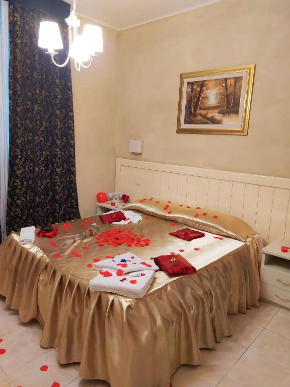 Romantiska guļamistaba ar zeltainu gultas veļu, rozā ziedlapiņām un siltu apgaismojumu, ideāla romantiskai vakaram. Eleganti dekorēta ar mākslas darbu uz sienas un drapējuma aizkariem.