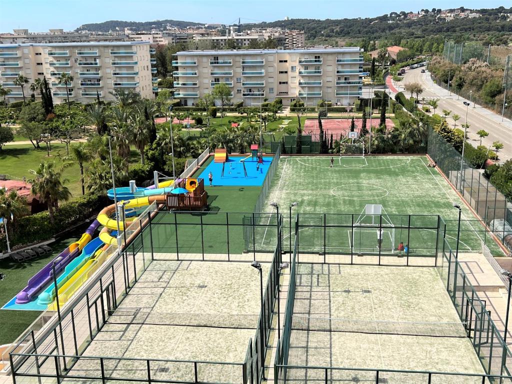 Sporta un atpūtas kompleksa skats ar futbola laukumu, bērnu spēļu laukumu un ūdens slidkalniņu. Apkārtne ir zaļa un labi kopta, ar daudziem augiem un ēkām.