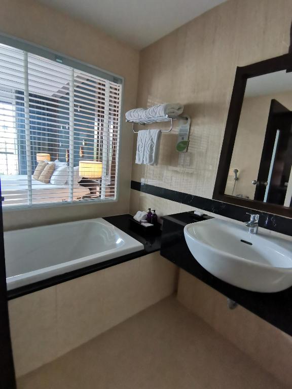 Mūsdienīgs vannas istabas interjers ar vannu un izlietni, kurā redzami dvieļi un spogulis. Aiz loga ir guļamistaba ar ērtu gultu un lampām.