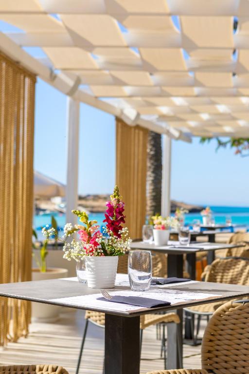 Saulaina pludmales kafejnīca ar galdiem, dekorētiem ar ziediem un skatu uz jūru. Ideāla vieta relaksācijai un ēdiena baudīšanai.