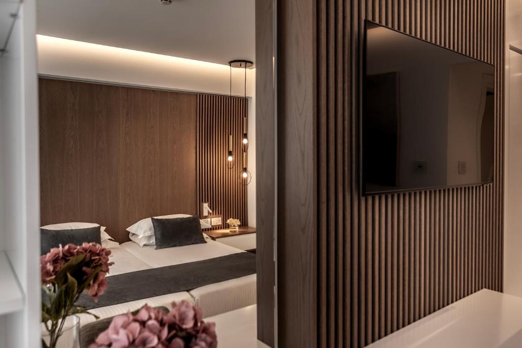 Mūsdienīgs viesnīcas numurs ar koka apdari un televizoru uz sienas. Gaismas elementi un ziedi papildina interjeru, radot patīkamu atmosfēru.