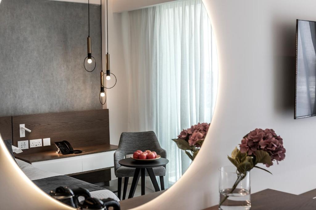 Mūsdienīgs viesnīcas numurs ar stilīgu interjeru, kurā redzami gaismas elementi, ērtas mēbeles un augļi uz galda. Gaismas tonis un logi rada patīkamu atmosfēru.