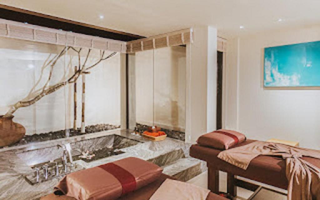 Mūsdienīgs spa interjers ar masāžas galdiem un relaksējošu atmosfēru, kurā redzams dabas elements un mākslas darbs uz sienas.