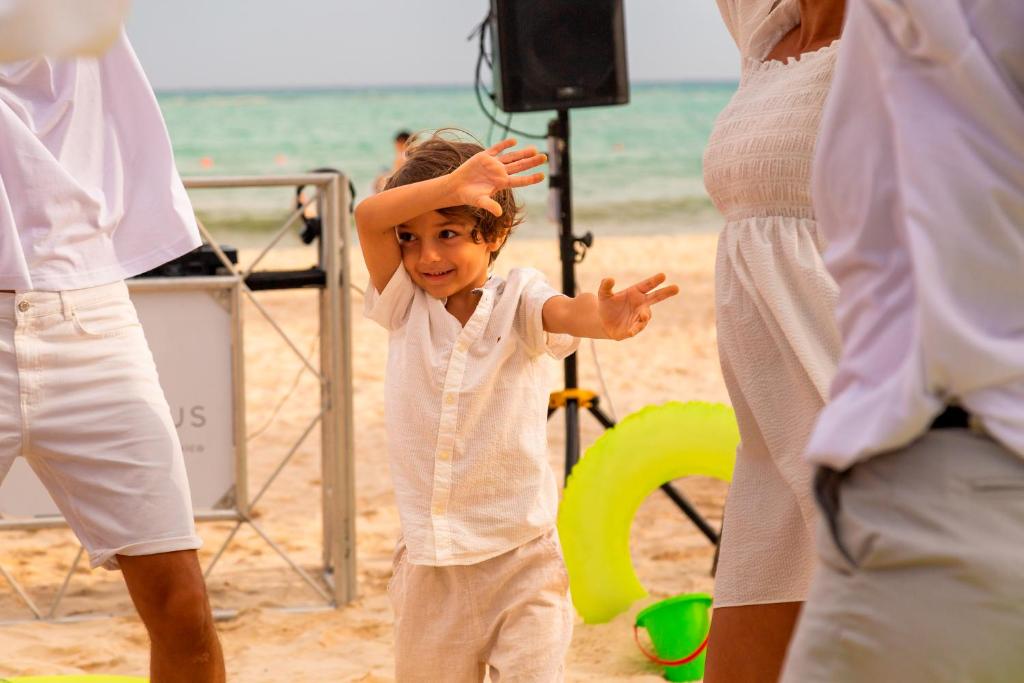 Bērns dejo pludmalē pie Paradisus Playa del Carmen, saulaina atmosfēra.