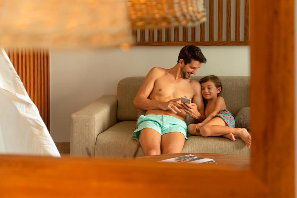 Tēvs un bērns atpūšas viesnīcā Paradisus Playa del Carmen, skatoties telefonu.