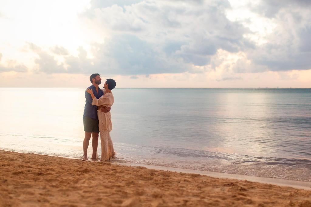 Pāris romantiskā mirklī pludmalē, stāvot uz smiltīm un skatoties viens otram acīs, ar saulrieta gaismu fonā.