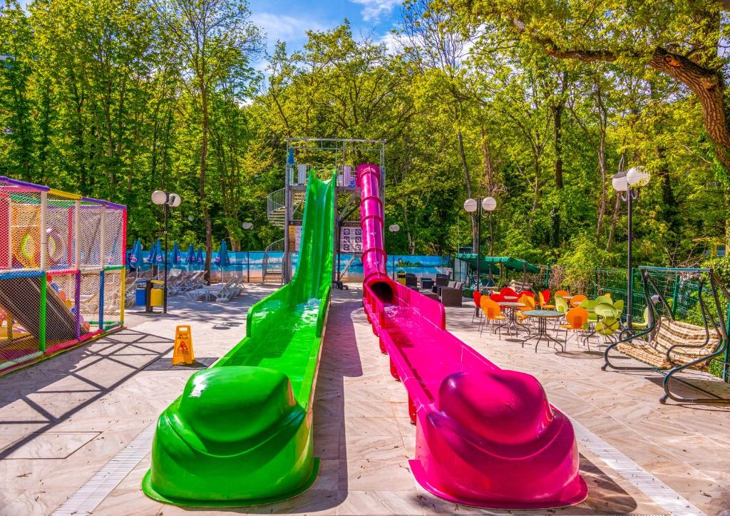 Krāsains ūdens slidkalniņš atradās zaļojošā parkā, ar dārza mēbelēm un saulainu debesu fona. Ideāla vieta izklaidei un atpūtai.