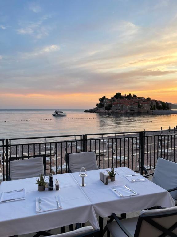 Romantisks skats uz jūru no restorāna terases, kur redzams kuģis un skaistā saulrieta ainava ar mazu salu.