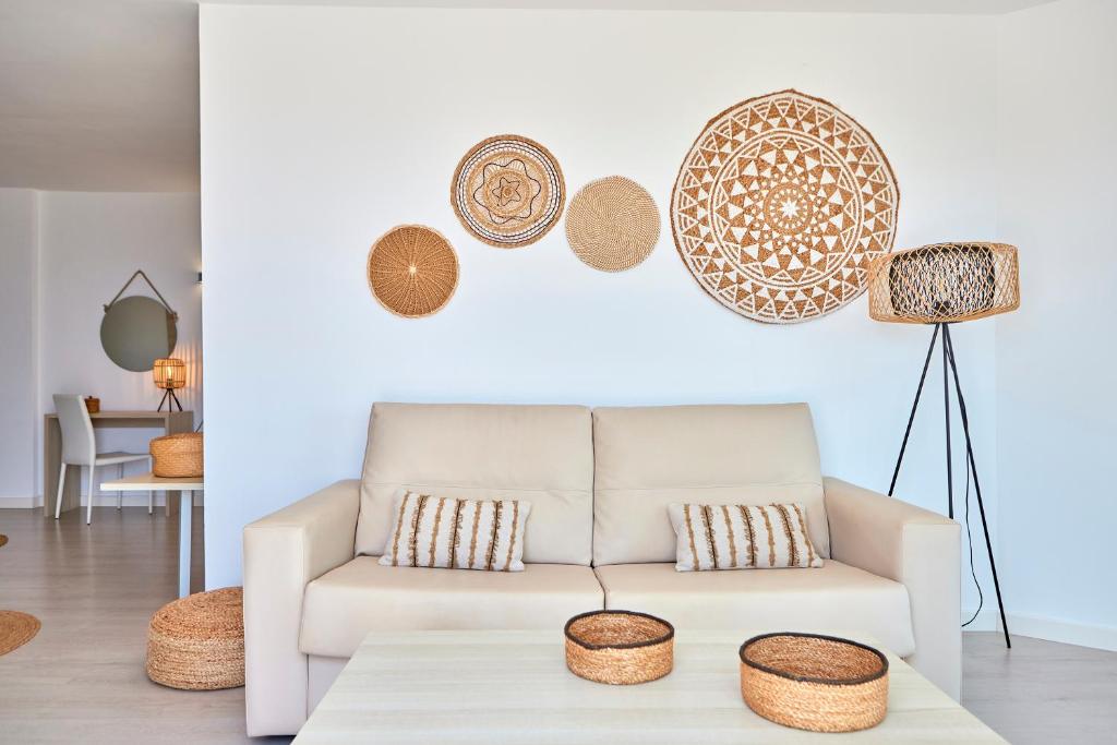 Mūsdienīgas viesistabas interjers ar neitrālām krāsām, kurā ir ērta dīvāns ar spilveniem un dekoratīviem groziem uz galda. Sienas rotā izstrādājumi no dabīgiem materiāliem, piešķirot telpai siltumu un mājīgumu.