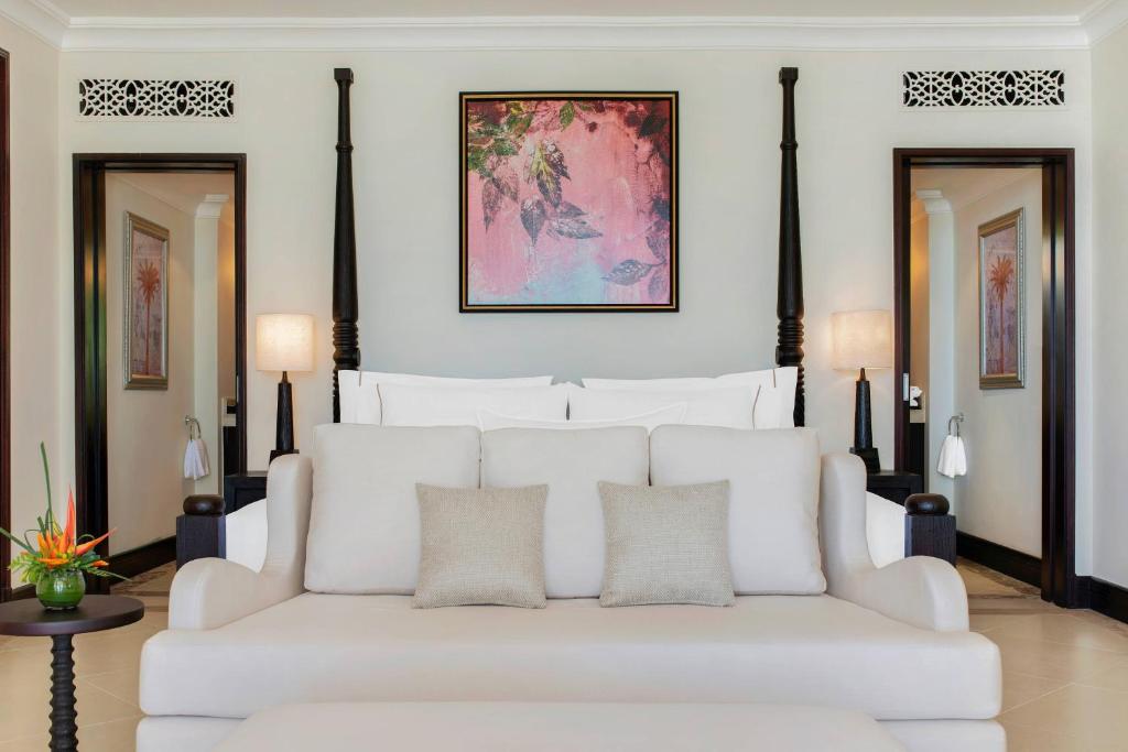 Mūsdienīga viesnīcas numura iekšskats ar gaišu dīvānu, dekoratīvu mākslas darbu uz sienas un mīkstām apgaismojuma ierīcēm. Interjerā ir redzami eleganti elementi un relaksējoša atmosfēra.