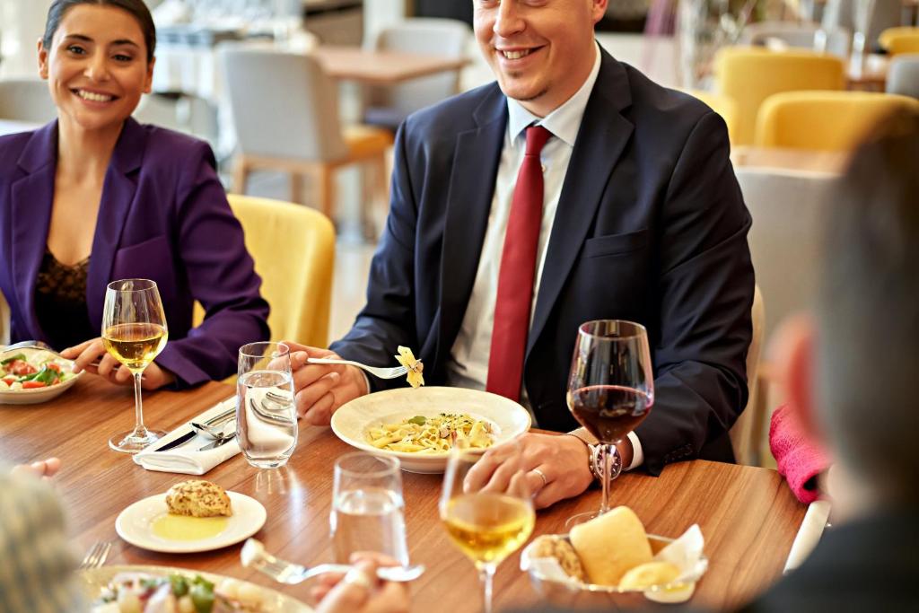 Elegants restorāns ar cilvēkiem, kas bauda maltīti un dzērienus. Uz galda redzama dažāda veida pārtika un vīns.