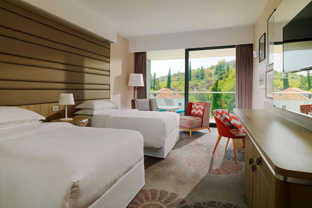 Mūsdienīga viesnīcas numura iekārtojums ar divām gultām, modernu mēbeļu komplektu un balkonu ar skatu uz dabu. Telpā ir arī dīvāns un televizors, radot relaksējošu atmosfēru.