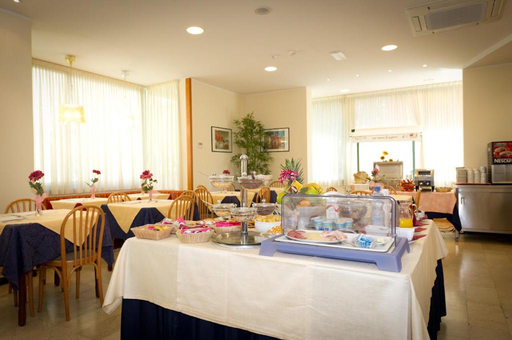 Brokastīm paredzēts galds ar dažādiem ēdieniem, tostarp augļiem, maizēm un dzērieniem, apkārt ir ēdamgaldi ar ziediem un brīnišķīgu apgaismojumu.