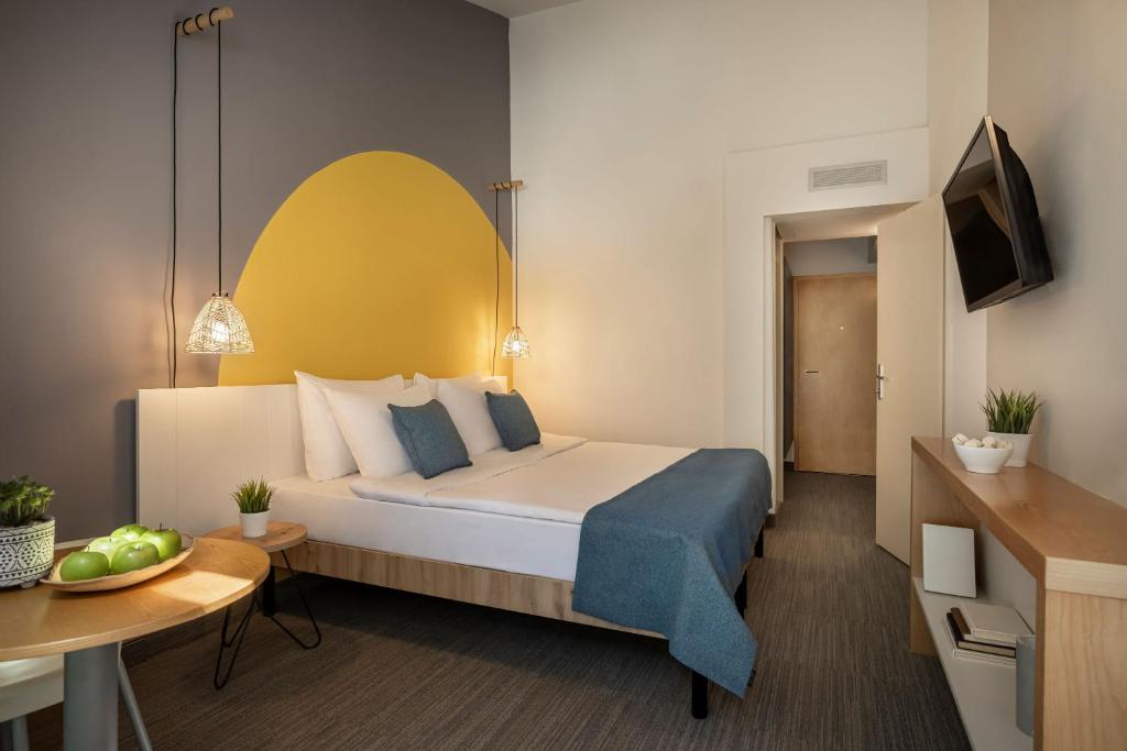 Mūsdienīgs viesnīcas numurs ar divguļamo gultu, spilveniem un dzeltenu sienu akcentu. Interjerā ir eleganta apgaismojuma sistēma un minimālistiska mēbele, radot mierīgu atmosfēru.